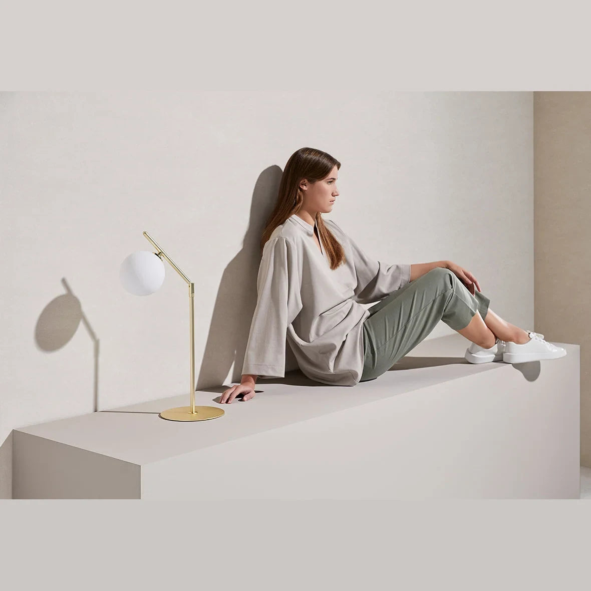 Adjustable arm opal glass globe lamp, on a ledge, beside a seated woman