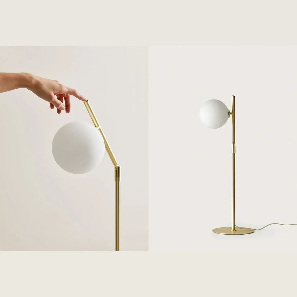 Adjustable arm opal glass globe lamp, in matte brass, being adjusted by hand