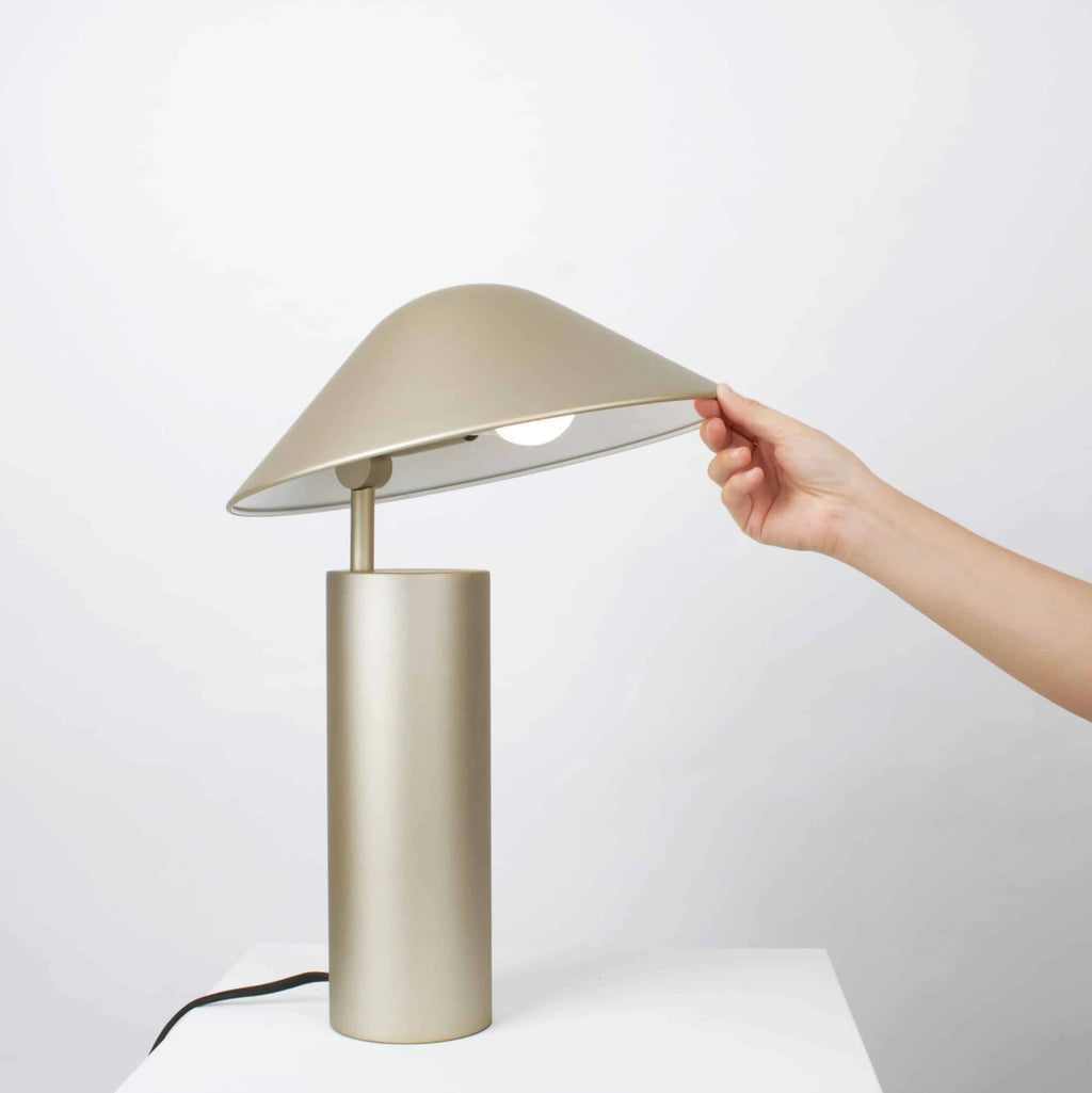 Adjustable cone shade steel table lamp, in Champagne Gold, a hand adjusting the shade