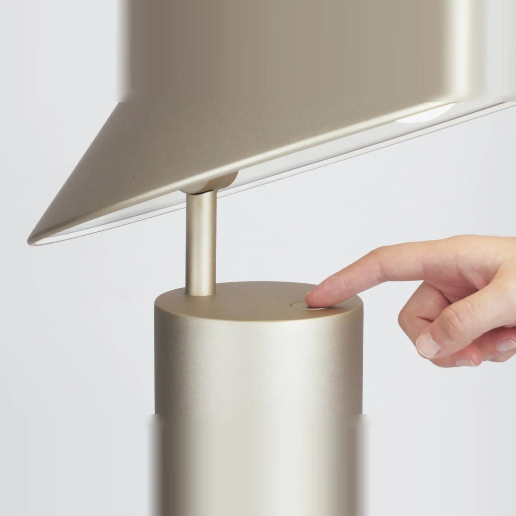 Adjustable cone shade steel table lamp, in Champagne Gold, a finger pressing the button