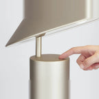 Adjustable cone shade steel table lamp, in Champagne Gold, a finger pressing the button