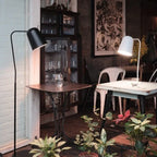 Adjustable shade steel floor lamp in black, beside a table in a dark room