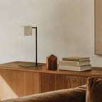 Alabaster cube table lamp with square stem, in matte black on a wooden sideboard