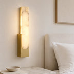 Alabaster panel wall light, in gold, lit beside a bed
