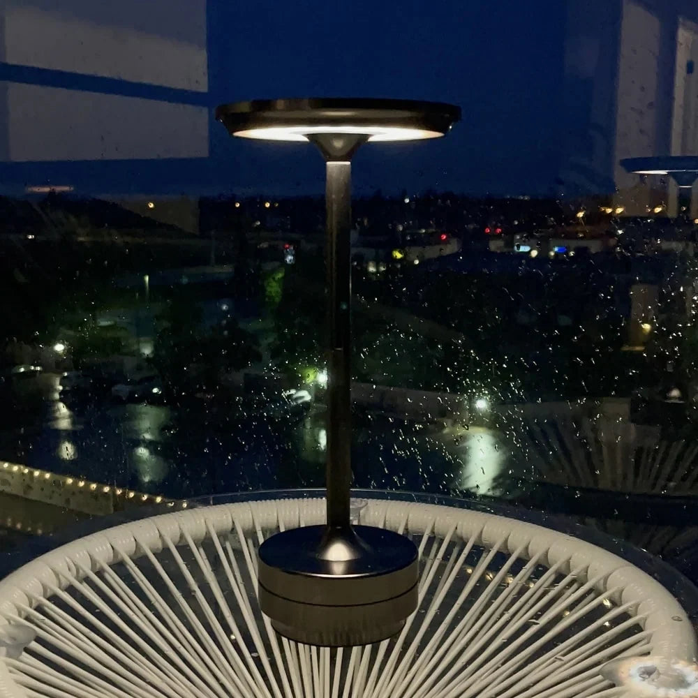 Aluminium cordless table lamp, lit on an outdoor table at night