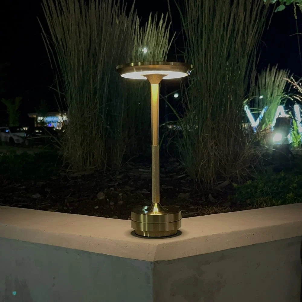 Aluminium cordless table lamp, lit outdoors beside plants