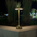 Aluminium cordless table lamp, lit outdoors beside plants