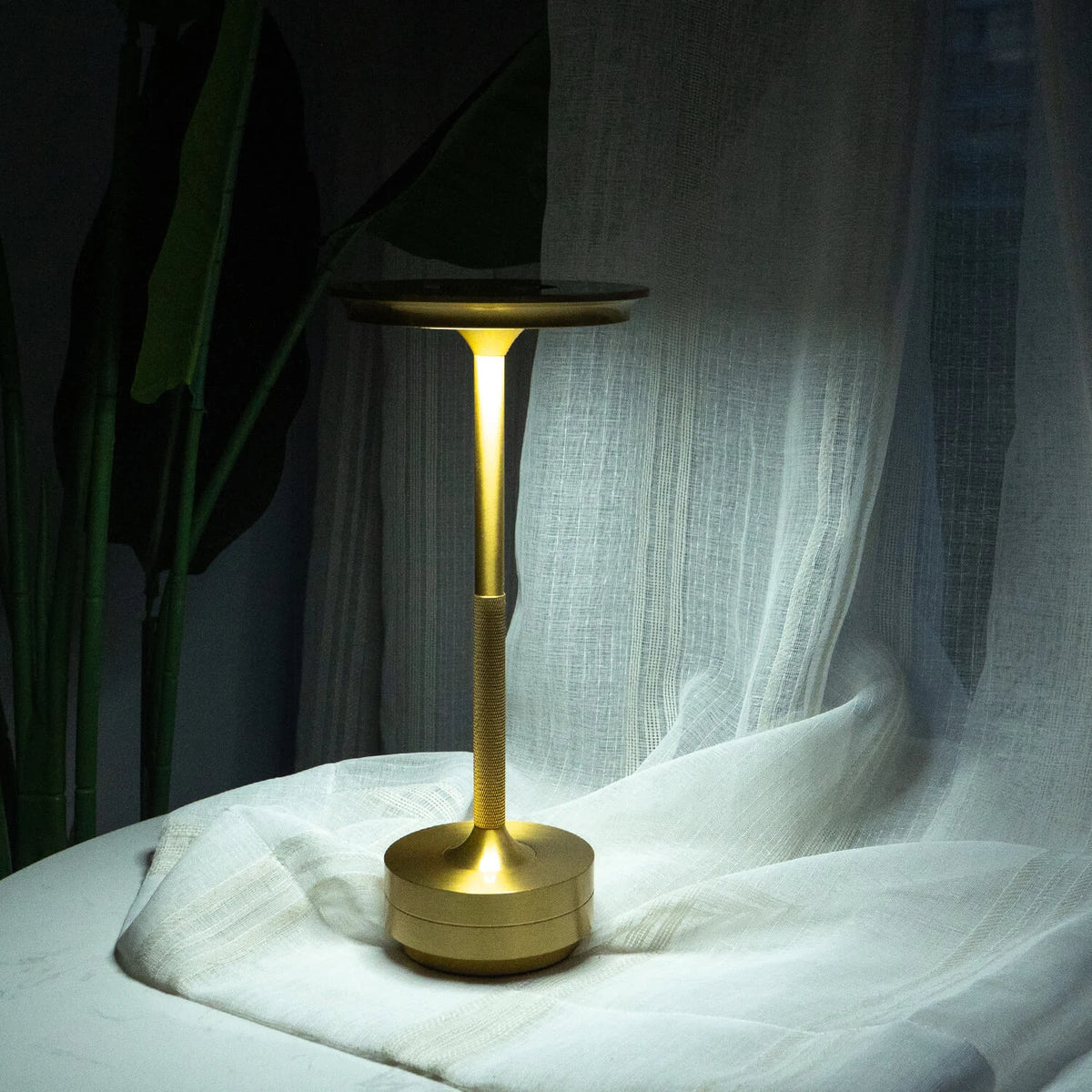Aluminium cordless table lamp, lit in a room setting