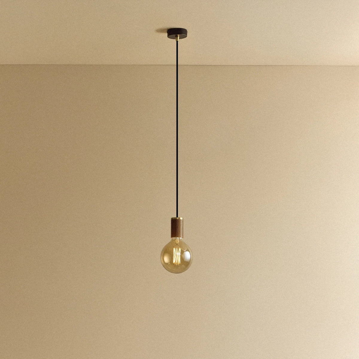 Amber Filament Globe Bulb Pendant, in walnut, lit, against a plain wall