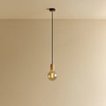 Amber tinted globe filament pendant, oak, lit, against a plain wall