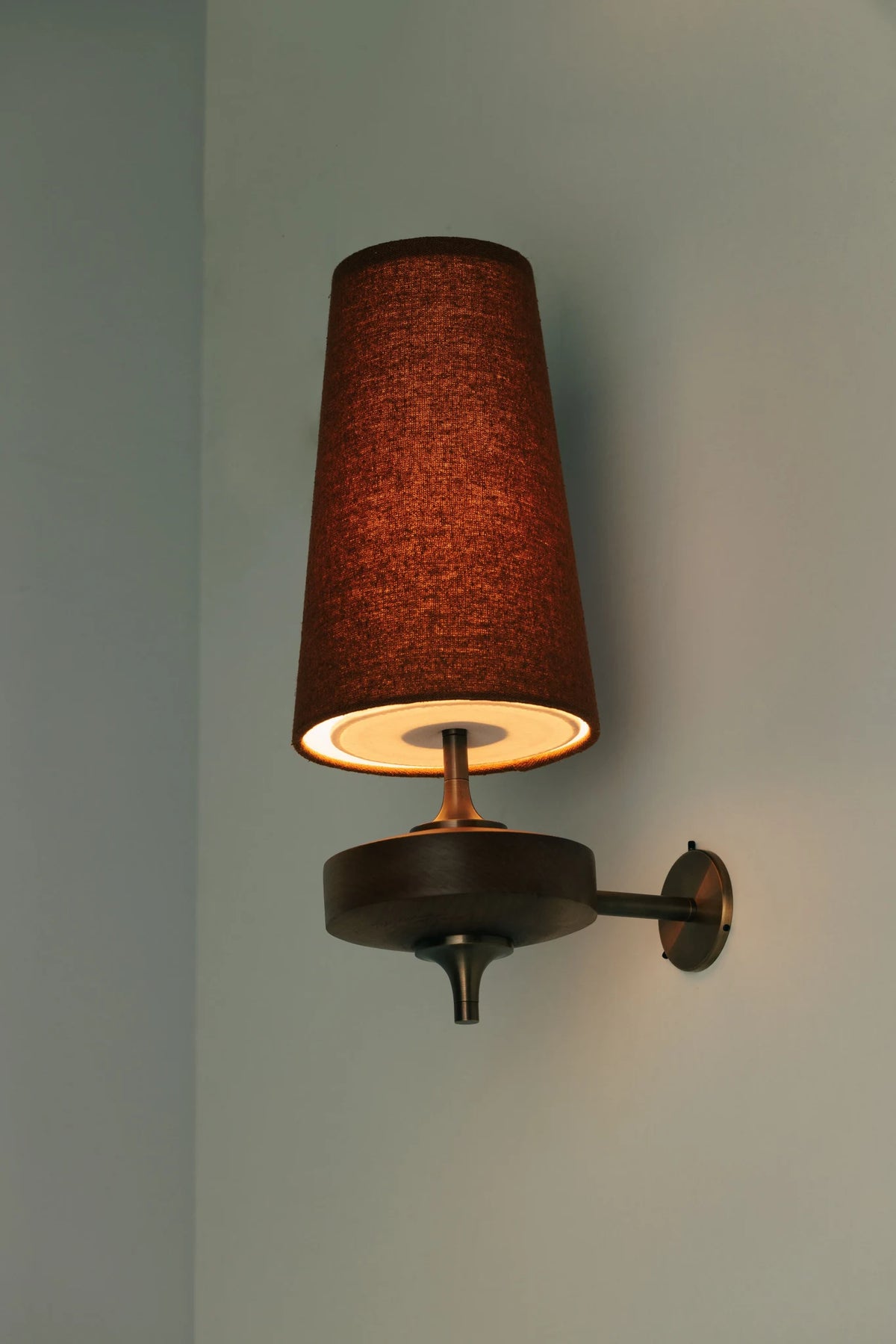 Walnut and antique brass wall light, lit, with a red shade