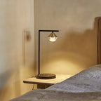 Black marble table lamp with a brass cone and optic glass diffuser, lit on a bedside table