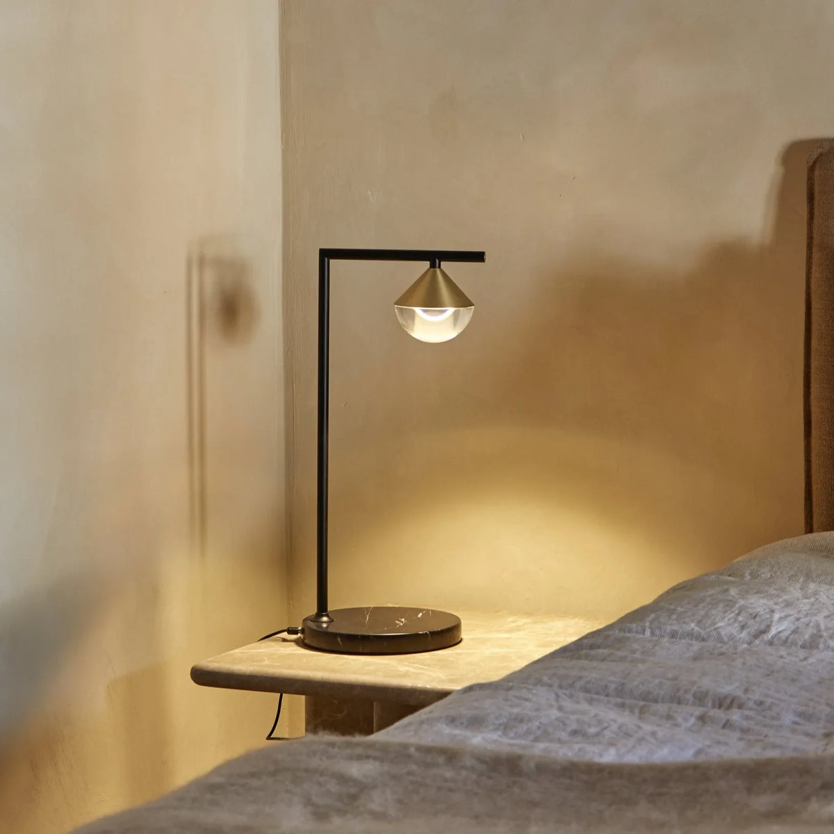 Black marble table lamp with a brass cone and optic glass diffuser, lit on a bedside table