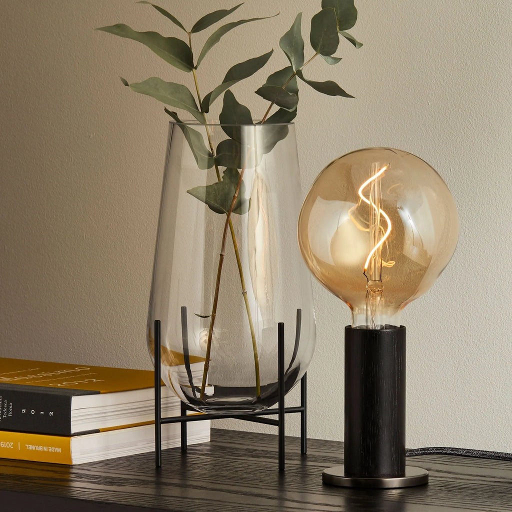 Blackened oak bulb holder table lamp, fitted with a large filament globe, beside a vase of eucalyptus