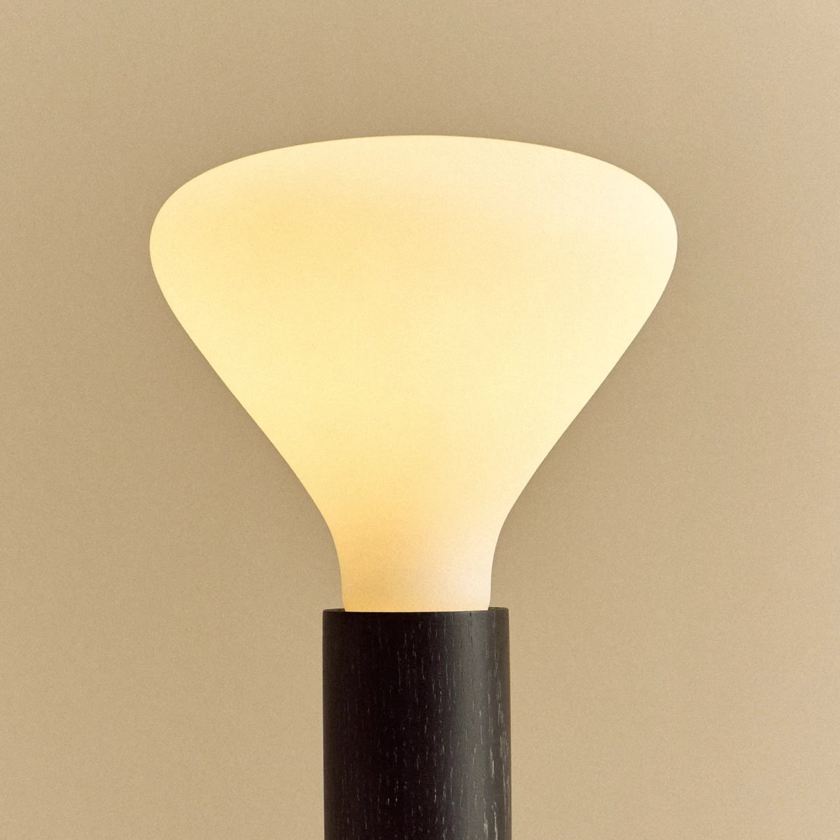 Blackened oak table lamp with a flared cone opal bulb, lit, close-up