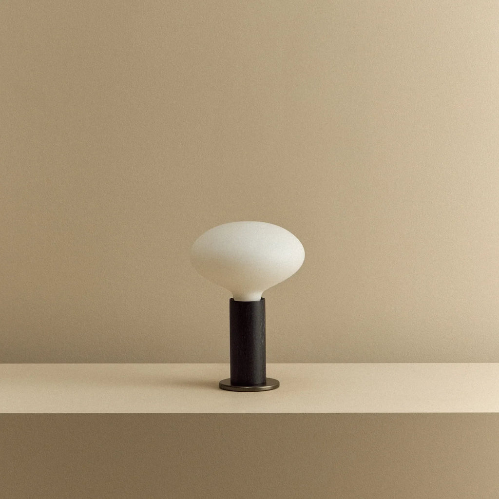 Blackened oak table lamp with a flat oval opal bulb, unlit, on a shelf
