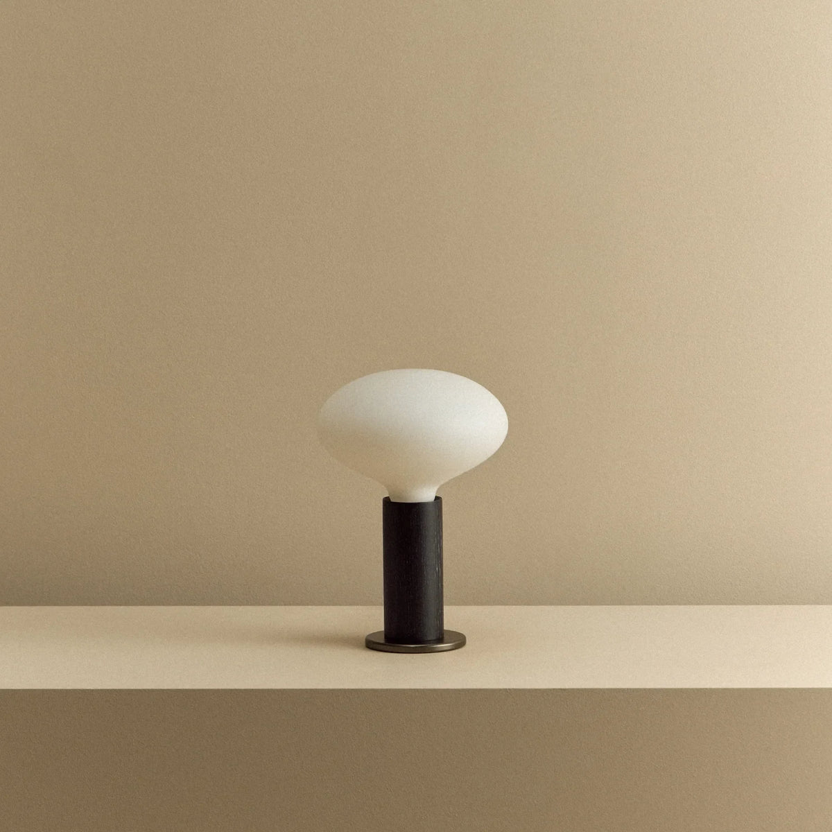 Blackened oak table lamp with a flat oval opal bulb, unlit, on a shelf