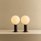 Blackened oak table lamp pair, opal globe bulbs, lit, together on a shelf