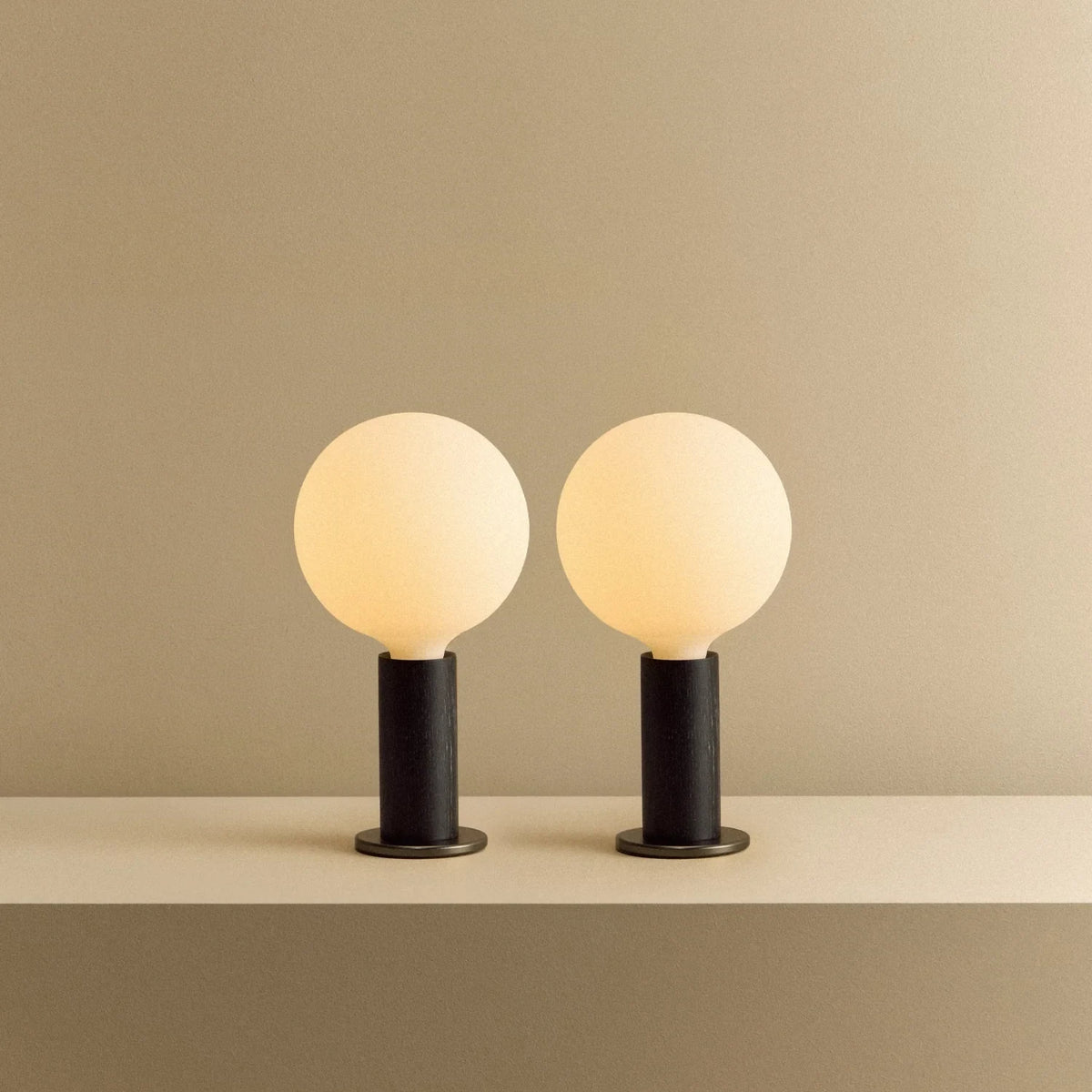 Blackened oak table lamp pair, opal globe bulbs, lit, together on a shelf
