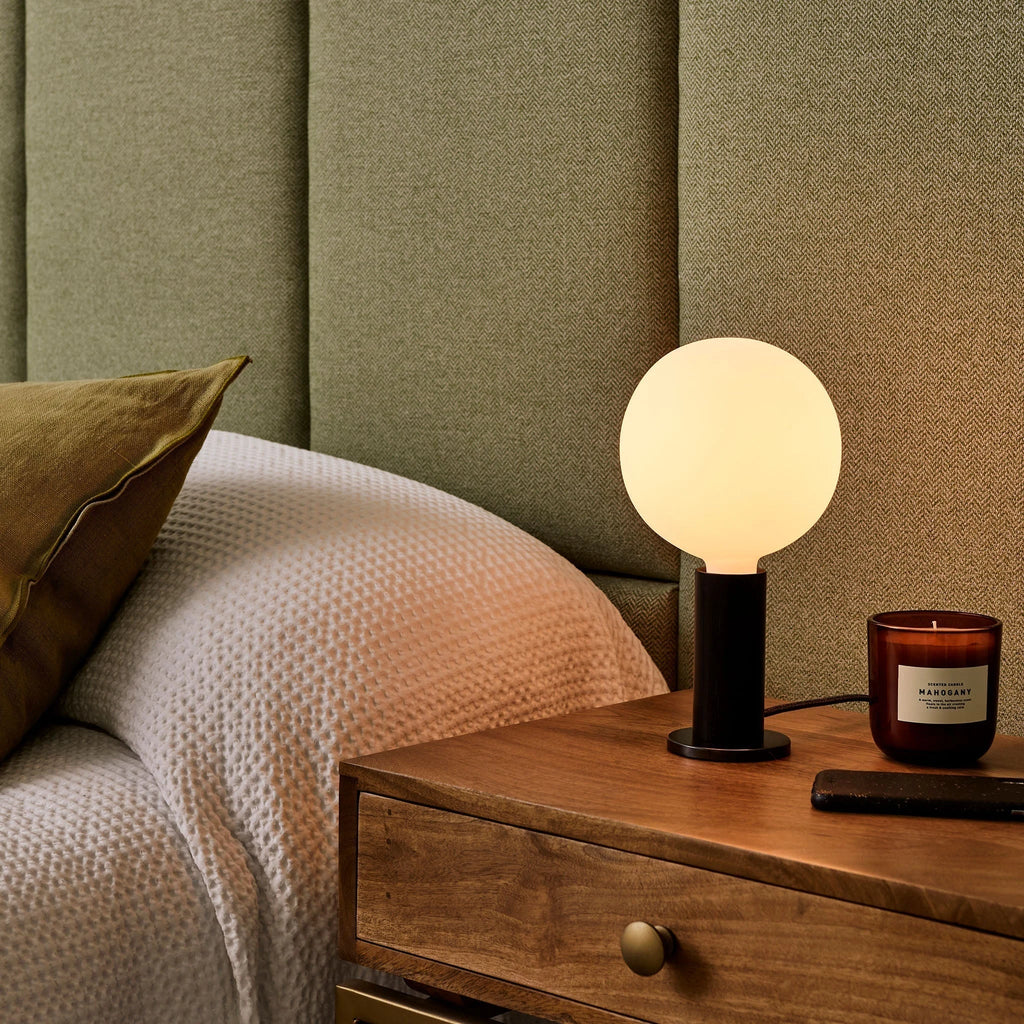 Blackened oak table lamp pair, opal globe bulbs, beside a bed