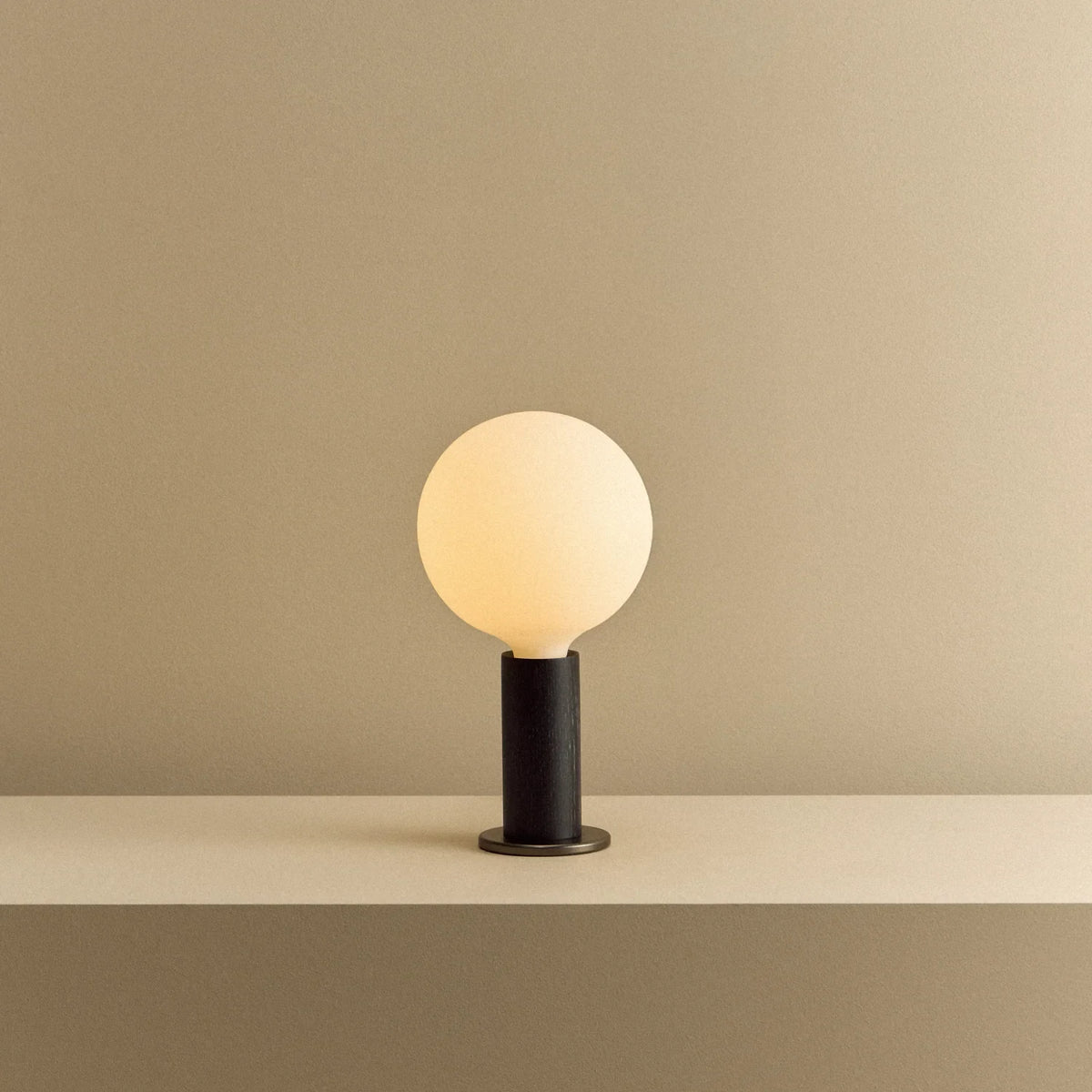 Blackened oak table lamp, opal globe bulb, lit, on a shelf