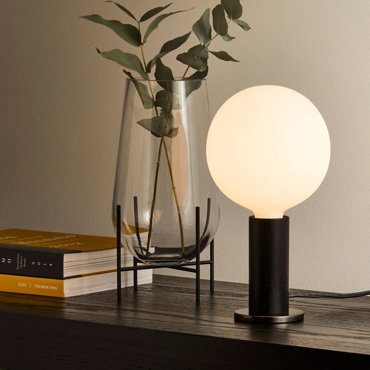 Blackened oak table lamp, opal globe bulb, on a dark sideboard beside the vase