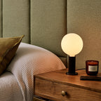 Blackened oak table lamp, opal globe bulb, beside a bed