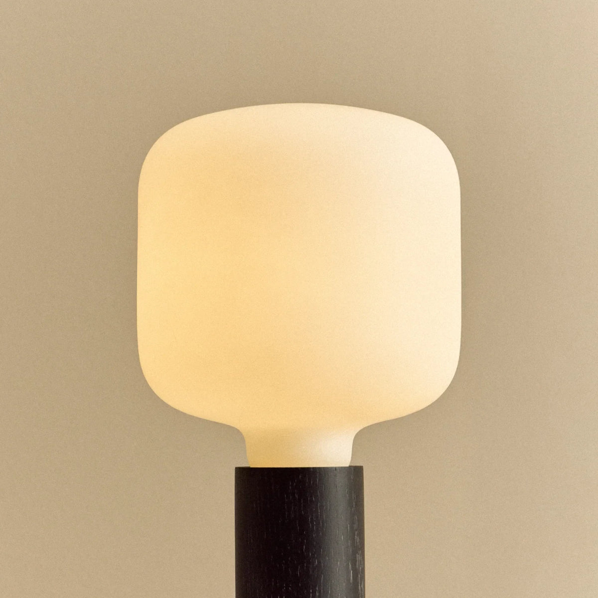 Blackened oak table lamp with a rounded square opal bulb, lit, close-up
