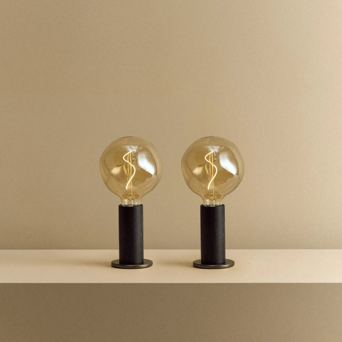 Blackened oak table lamp pair, tinted globe bulbs, lit, together
