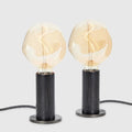 Blackened oak table lamp pair, tinted globe bulbs, on a white background
