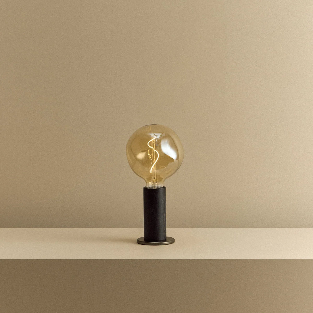 Blackened oak table lamp, tinted globe bulb, lit, on a shelf