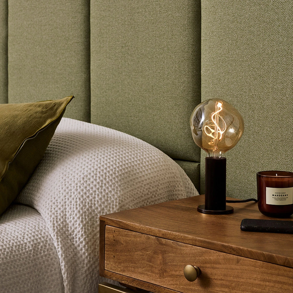 Blackened oak table lamp, tinted globe bulb, on a bedside chest