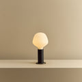 Blackened oak table lamp with a trapezoid opal bulb, lit, on a shelf