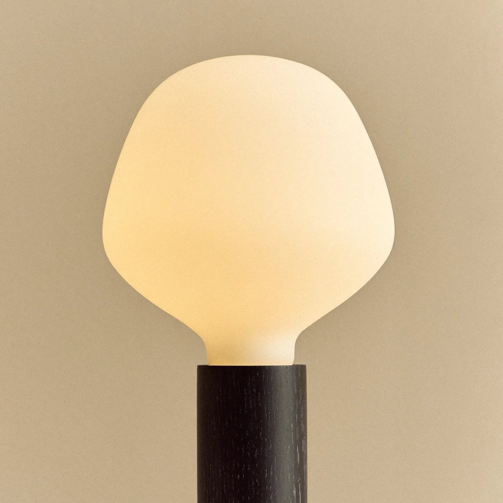 Blackened oak table lamp with a trapezoid opal bulb, lit, close-up