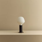 Blackened oak table lamp with a trapezoid opal bulb, unlit, on a shelf