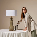 Bottle-shaped glass table lamp, on a draped table, with a shade (not included)