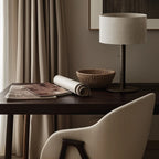 Braided leather column table lamp with drum shade, on a wooden desk beside a chair