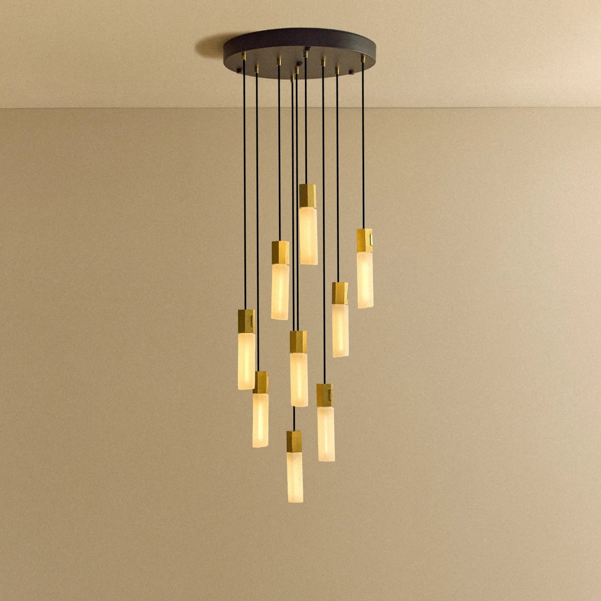 Nine-drop cluster pendant in cast brass with glass bulbs, lit, against a plain wall