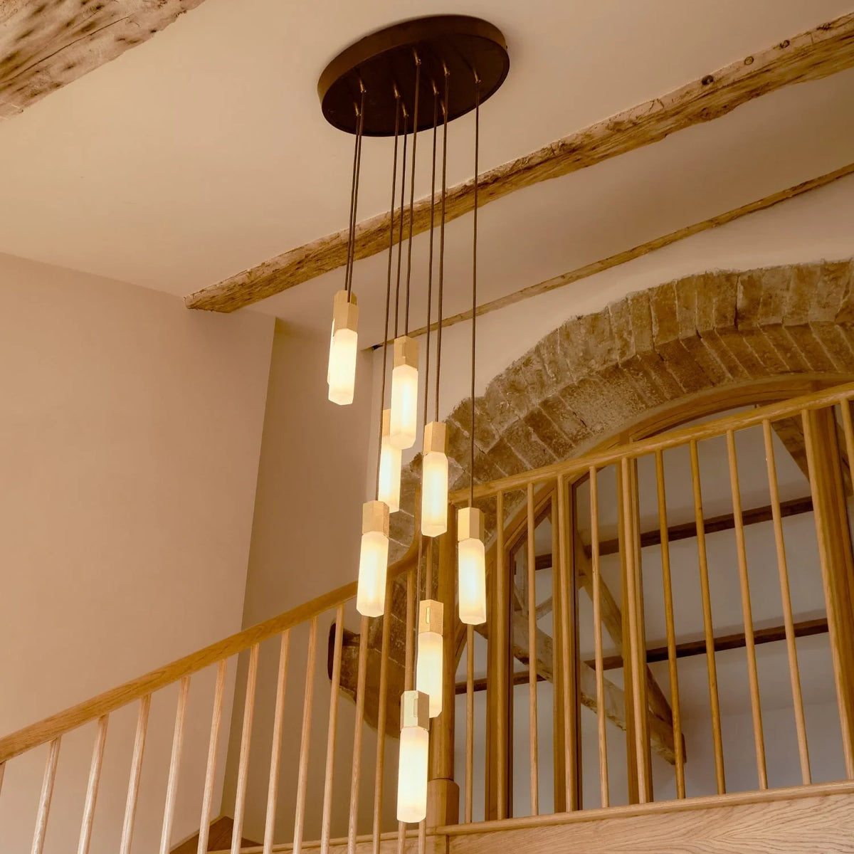 Nine-drop cluster pendant in cast brass with glass bulbs, above a staircase