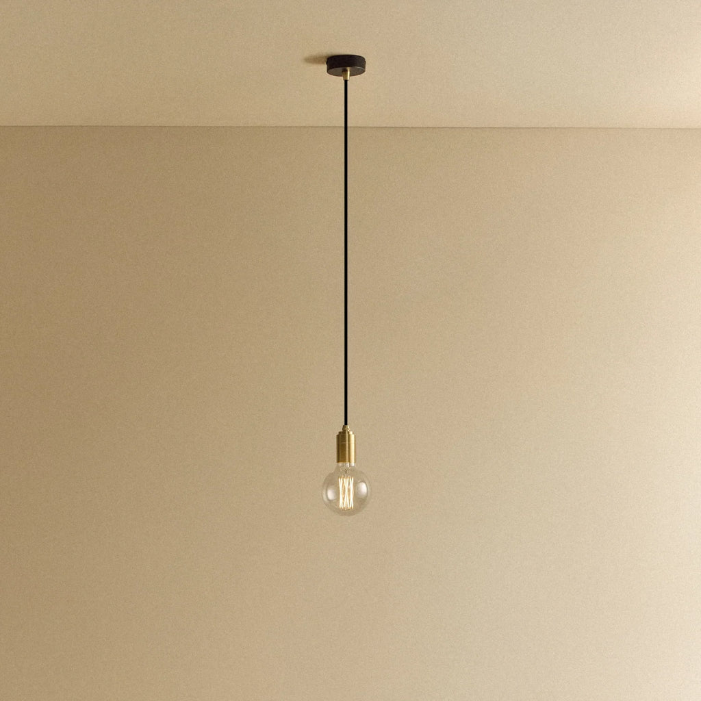 Brass pendant with non-tinted glass filament bulb, lit, against a plain wall