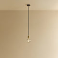 Brass pendant with non-tinted glass filament bulb, lit, against a plain wall