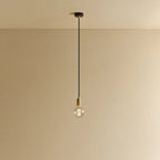 Brass pendant with non-tinted glass filament bulb, lit, against a plain wall
