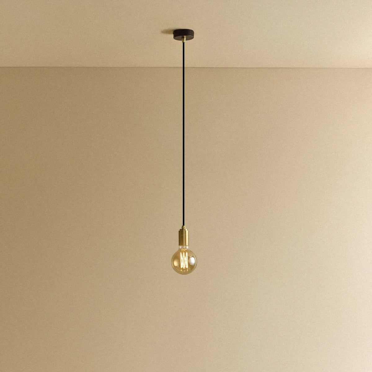 Brass pendant with tinted glass filament bulb, lit, against a plain wall
