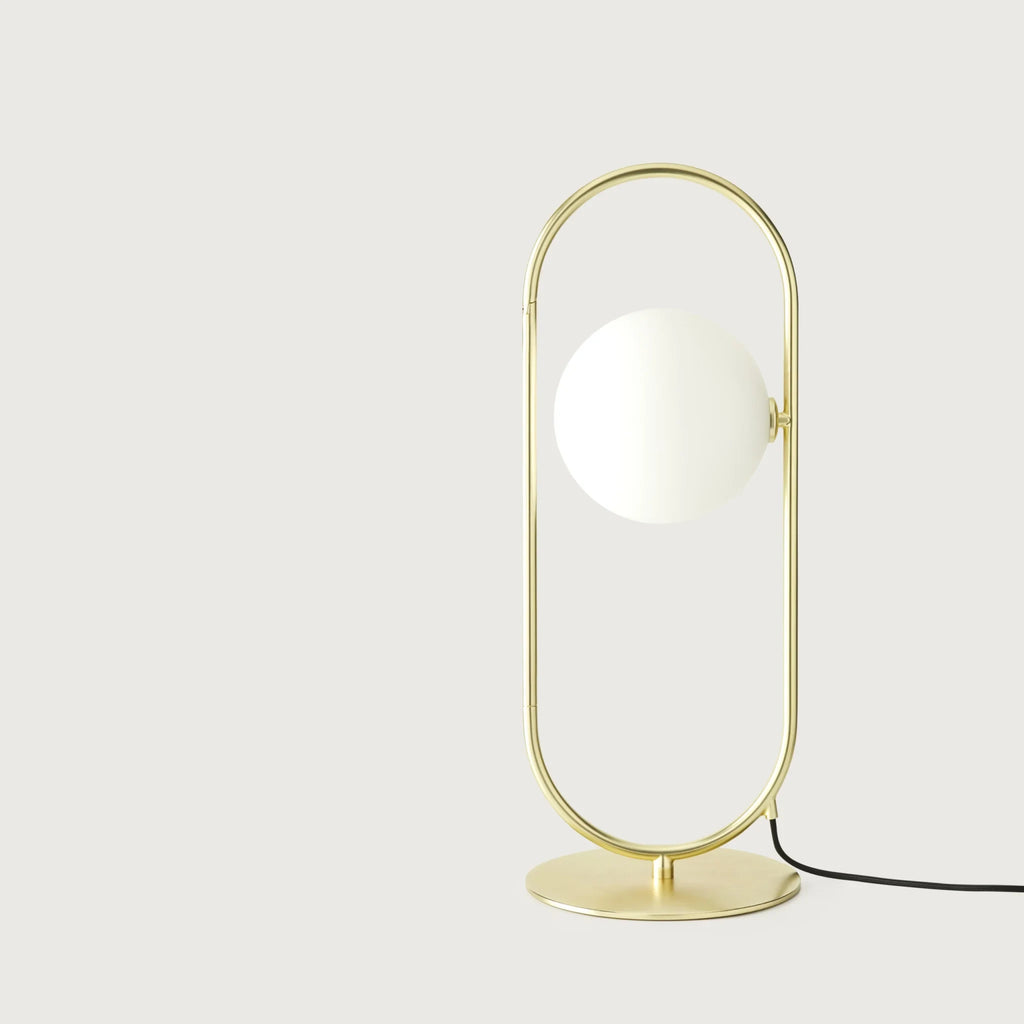 Brass ring table lamp with an opal glass globe, on a plain background