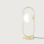 Brass ring table lamp with an opal glass globe, on a plain background