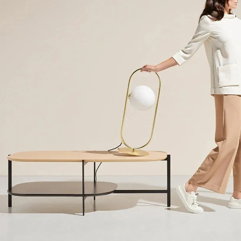 Brass ring table lamp with an opal glass globe, being carried across a room