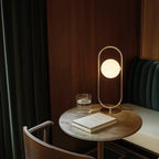 Brass ring table lamp with an opal glass globe, on a round table beside a book