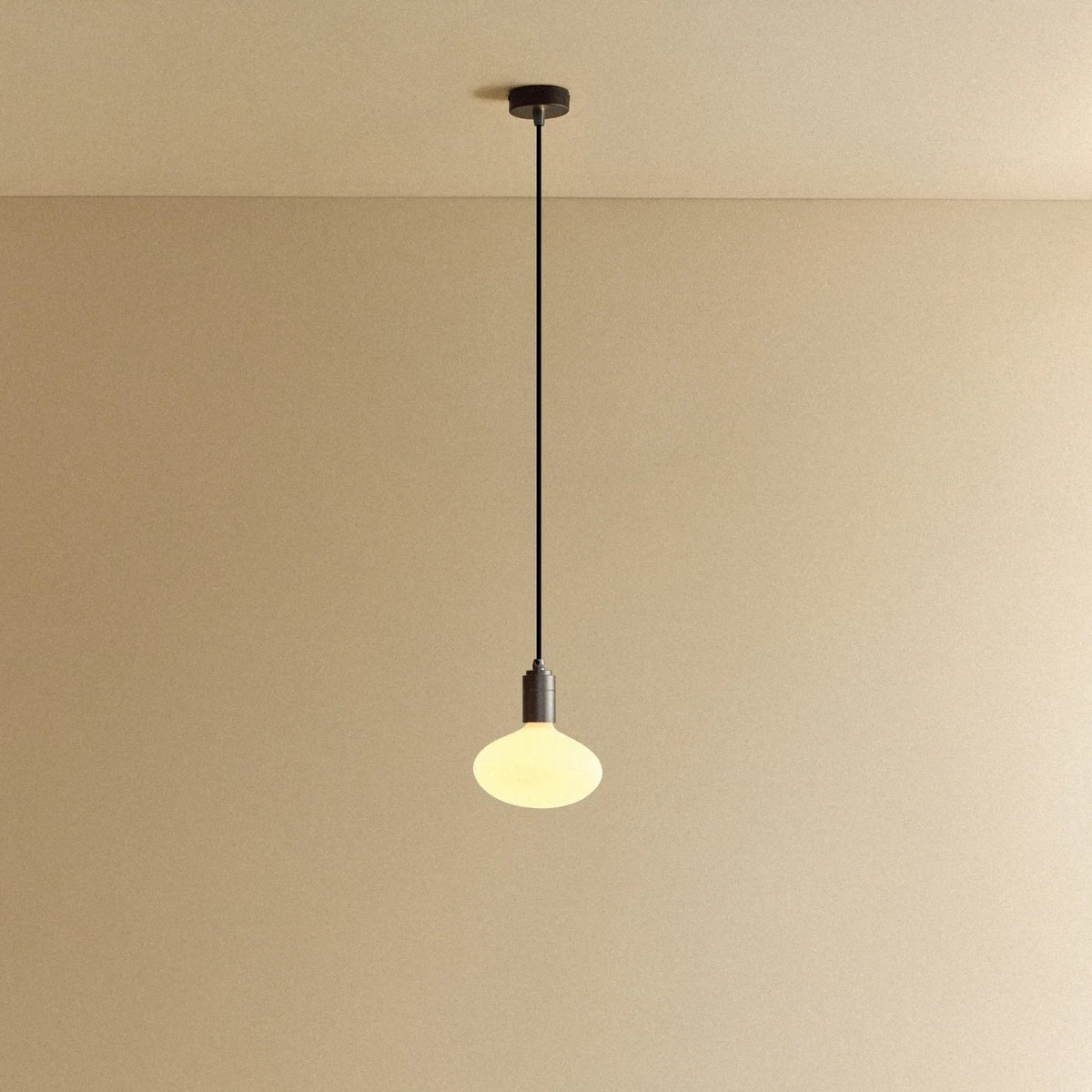 Broad dome matte white glass pendant, graphite, lit, against a plain wall
