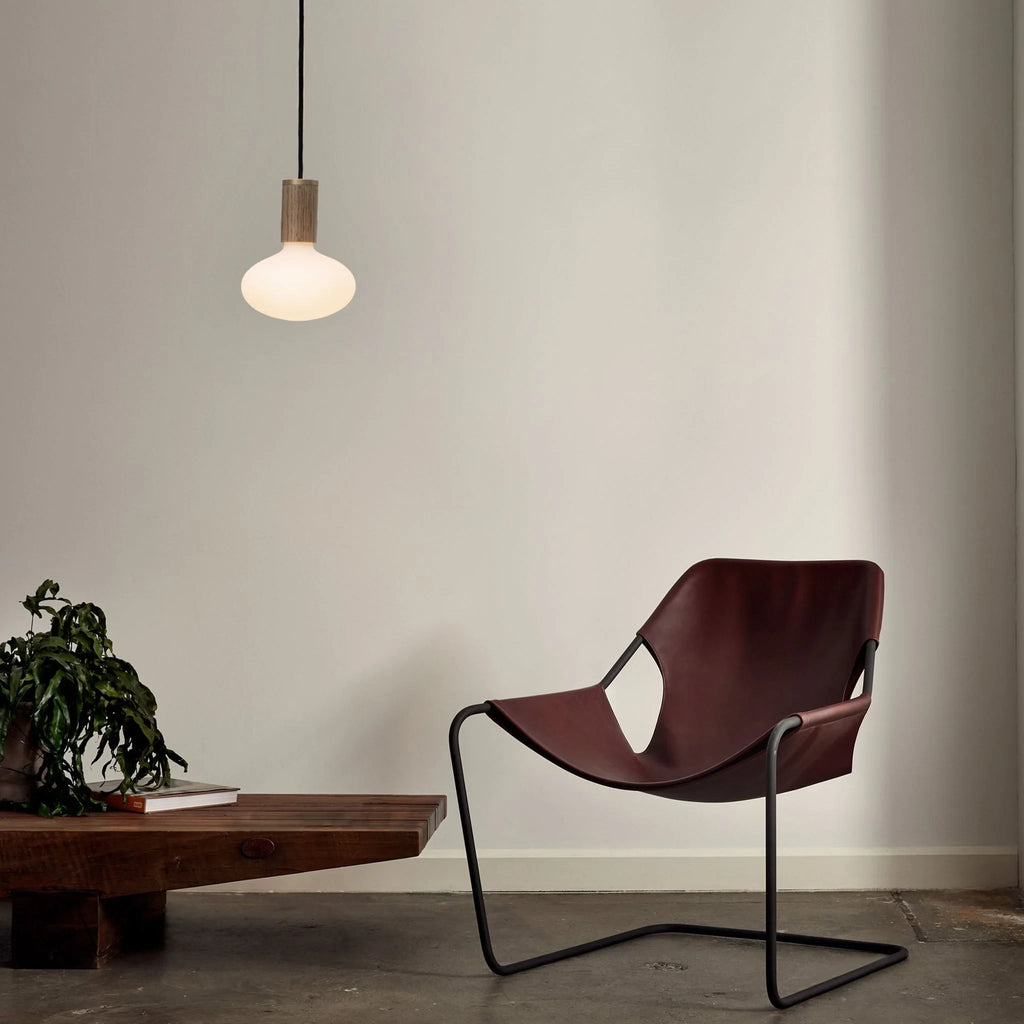 Broad dome matte white glass pendant, graphite, above a lounge chair