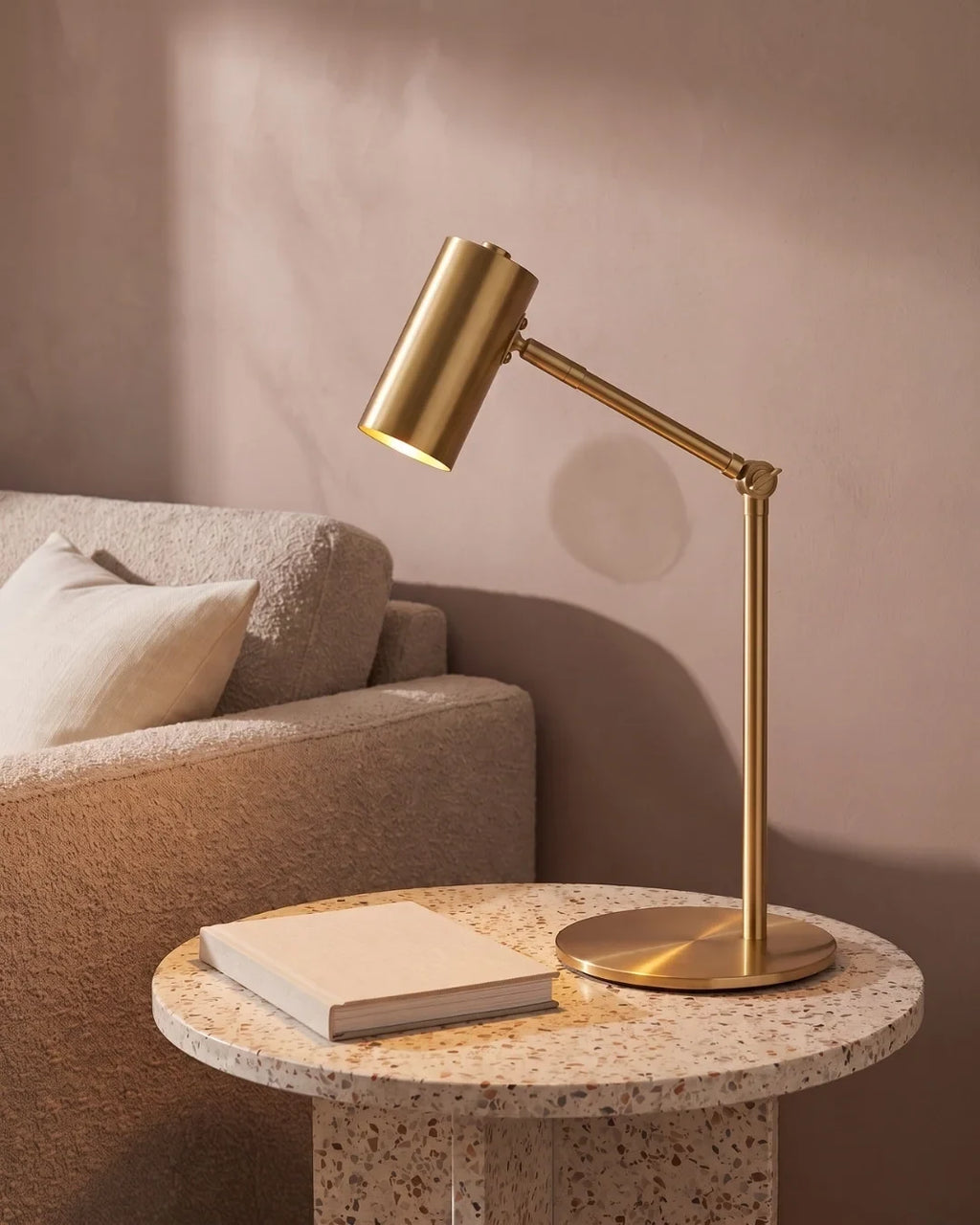 Brushed gold desk lamp with an adjustable arm, on a round side table